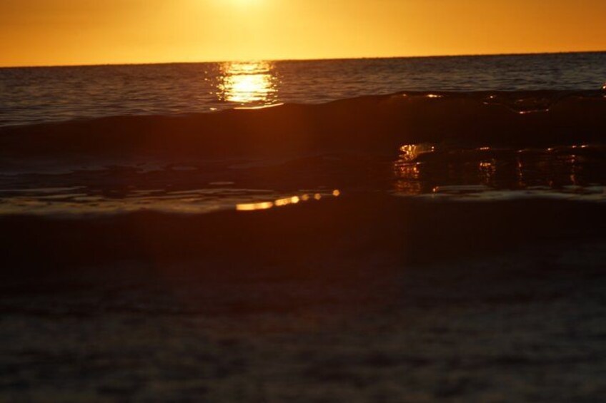 A sunset over the ocean with waves and a rocky outcrop reflecting the sun. 3