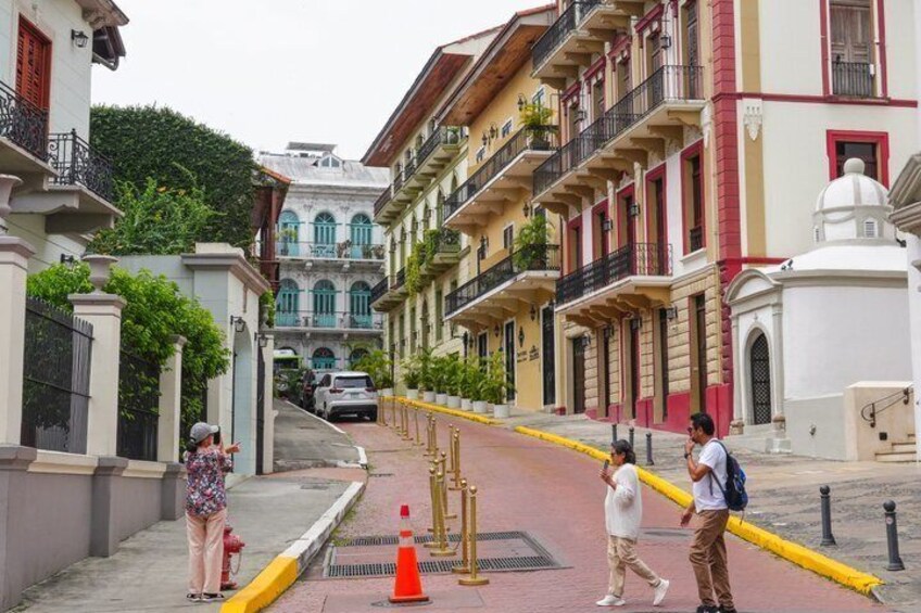 A street with buildings, a yellow barrier, and a person walking. 4