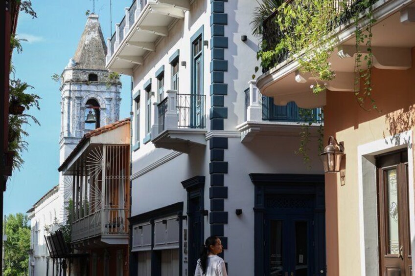 A street with buildings, a bell tower, and a person walking. 2