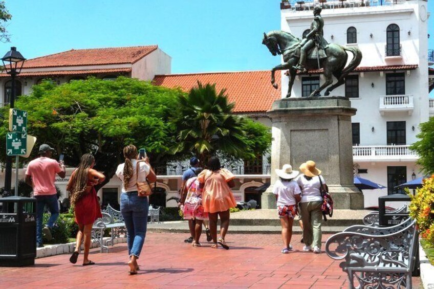 A statue of a man on horseback, people walking, and a building with a red roof. 5