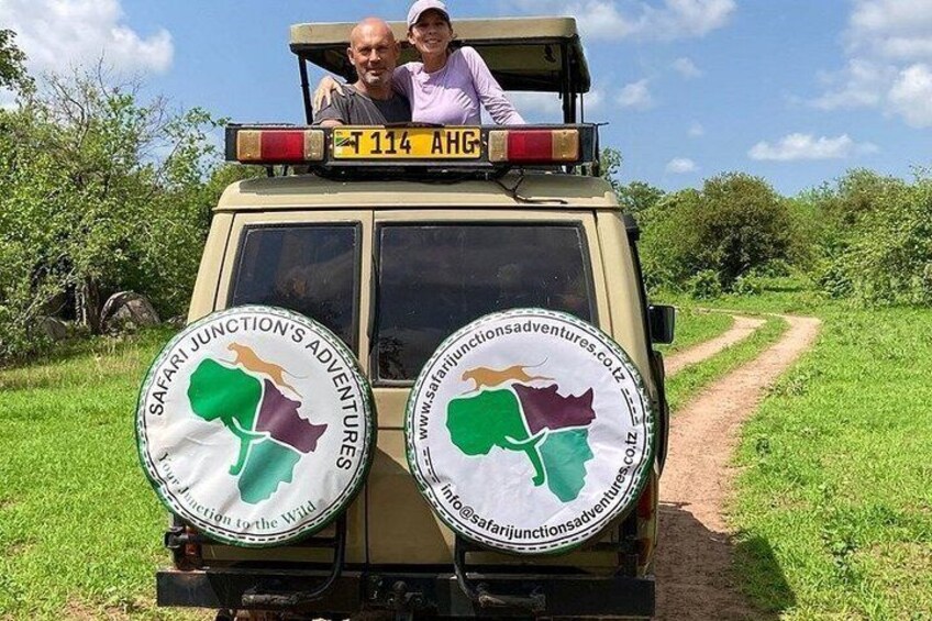 A safari vehicle with two circular stickers on the back, a road, and greenery. 1