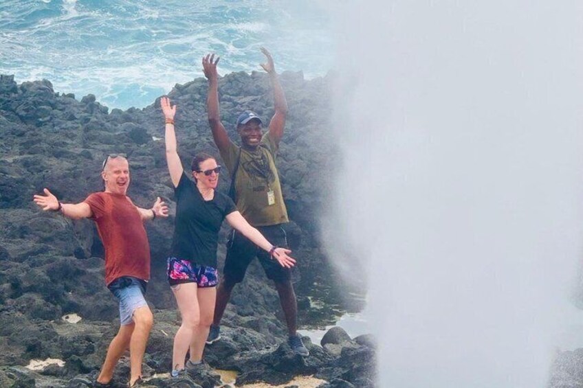 Three people standing on rocky terrain near a body of water with waves. 3