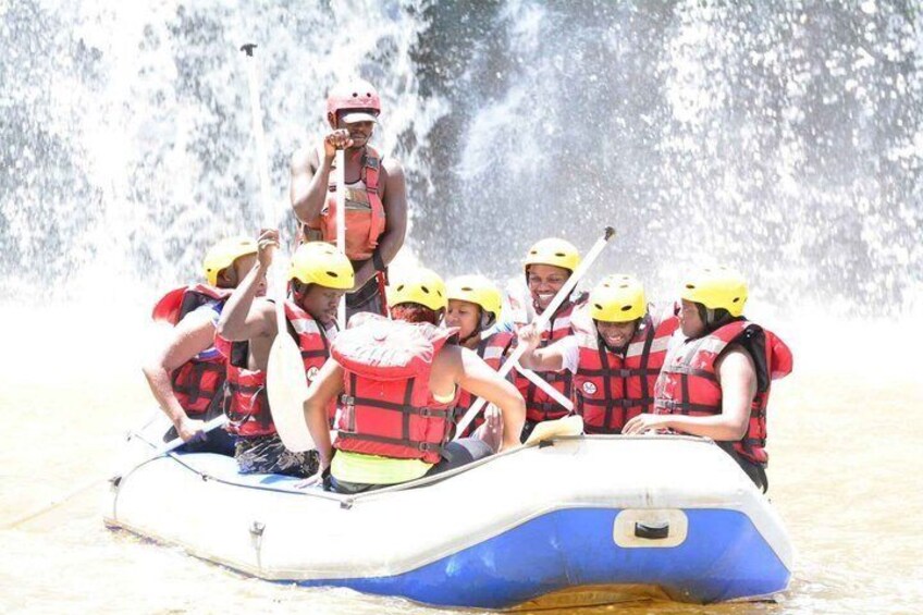 A group of people in a raft wearing life jackets and helmets, navigating through a water body. 2