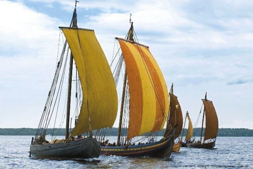 A row of traditional sailing boats with large sails on calm water. 4