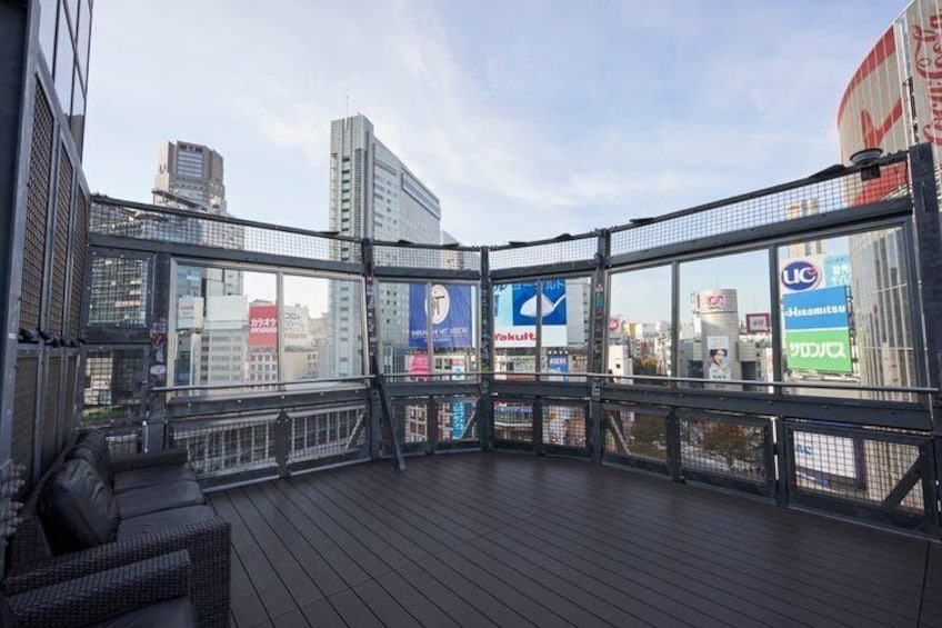 A rooftop terrace with a view of city buildings, a glass railing, and a wooden deck. 5