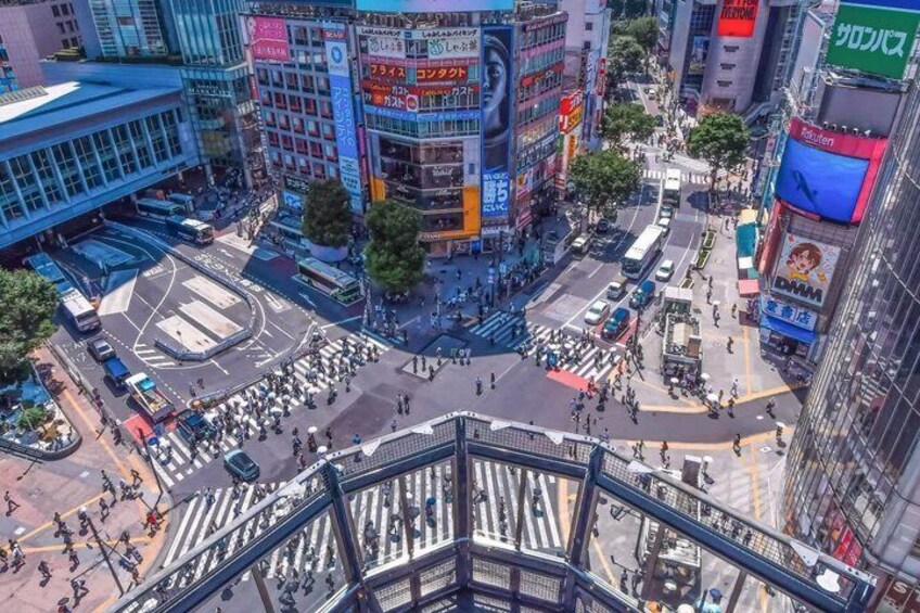 A busy urban intersection with multiple lanes and traffic signals, surrounded by tall buildings with various advertisements. 4