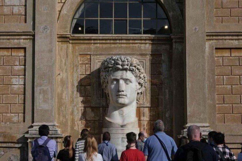 A classical bust sculpture in front of a building with arched windows and brick walls. 4
