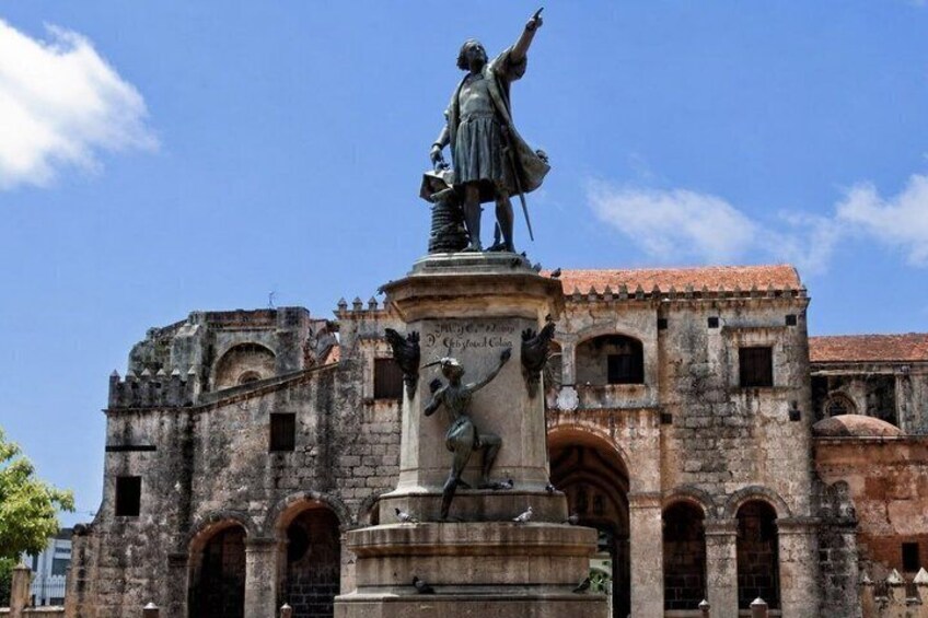 A statue on a pedestal in front of an old building with arched windows and a tiled roof. 3