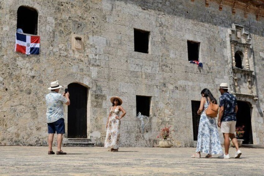 A stone building with arched doorways, a flag, and people posing for a photo. 2