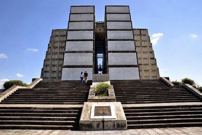 A large, modern building with a symmetrical design, featuring a central entrance flanked by two tall, rectangular structures. 1