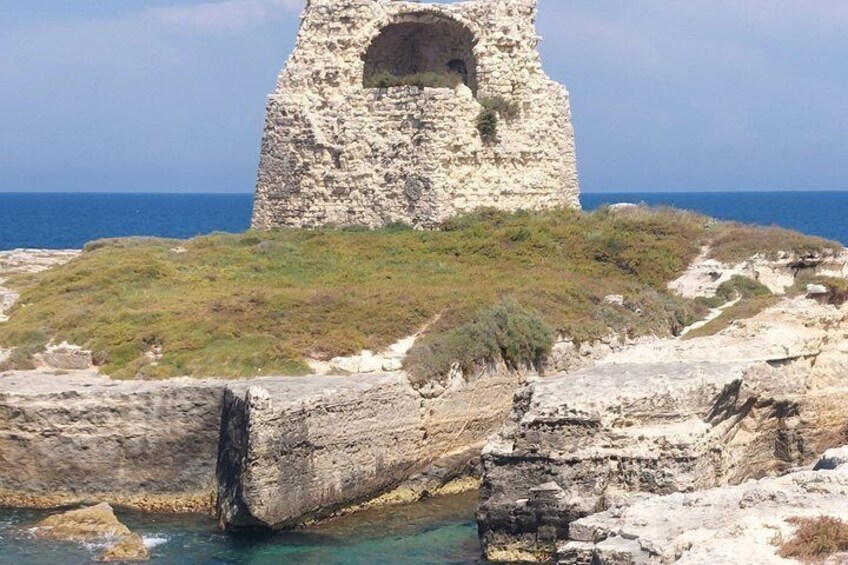 A stone tower, rocky coastline, and clear blue sea. 2