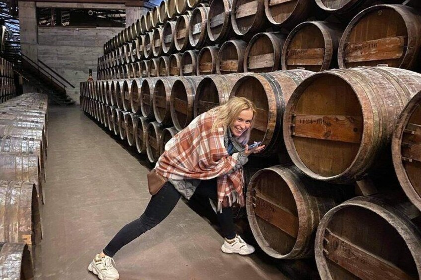 A person crouching in a warehouse with rows of wooden barrels. 4