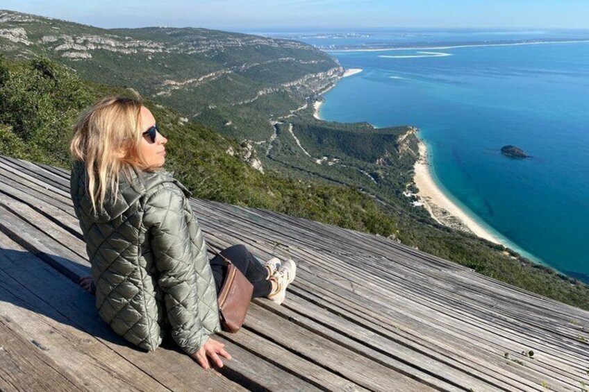 A person sitting on a wooden deck overlooking a coastal landscape with a beach and cliffs. 3