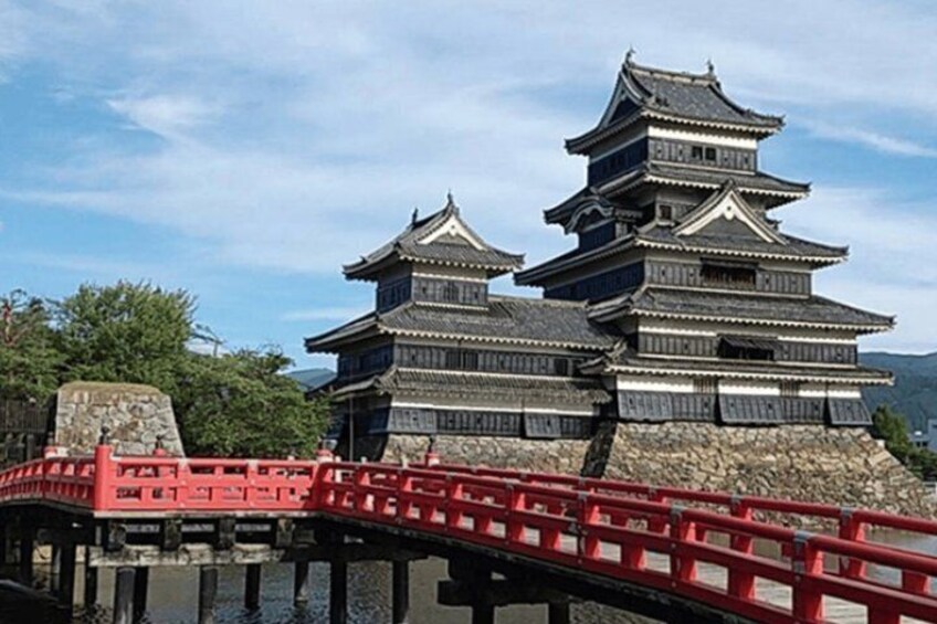 A traditional Japanese castle with multiple tiers, a red bridge in the foreground, and a clear sky. 4