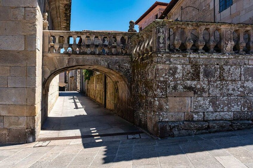 An old stone archway leading through a narrow alleyway, with a stone wall on one side and a building on the other. 4