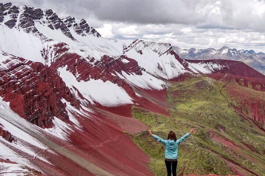 A person standing with arms raised, overlooking a valley with red and white mountains. 2