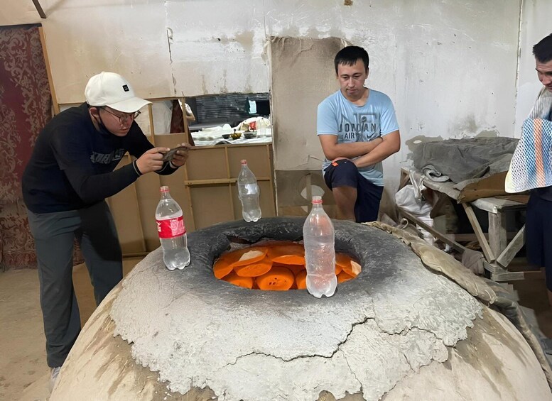 A group of people around a traditional oven with pizza dough and bottles of water. 4