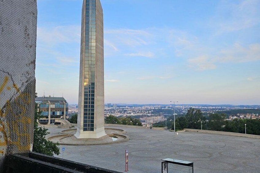 A tall glass skyscraper with a circular base, surrounded by a large open plaza. 3