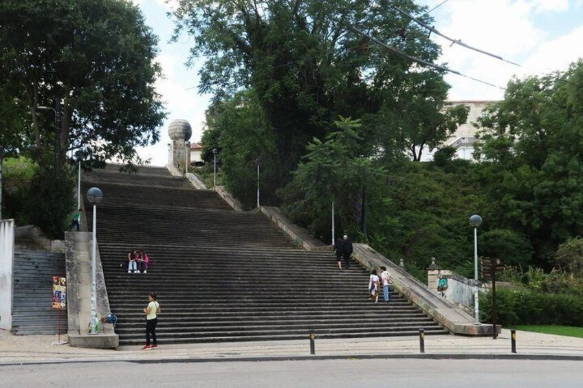 A set of stairs leading up to a building with a spherical structure on top, surrounded by trees and greenery. 3
