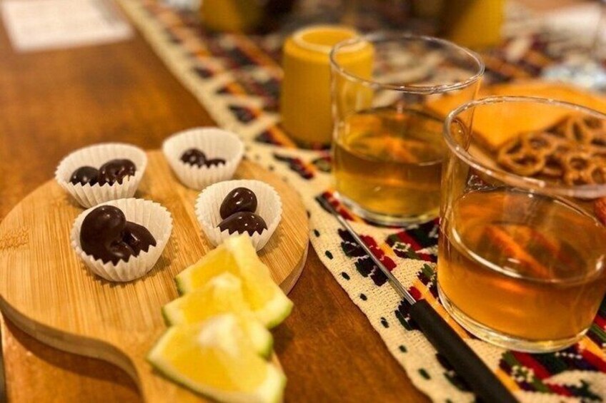 A wooden board with chocolate-covered items, a glass of amber liquid, and a slice of lime. 2