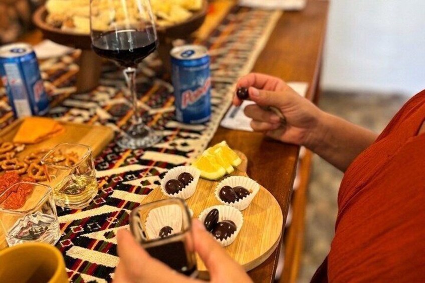 A person playing a wooden board game at a table with snacks, drinks, and a glass of wine. 1