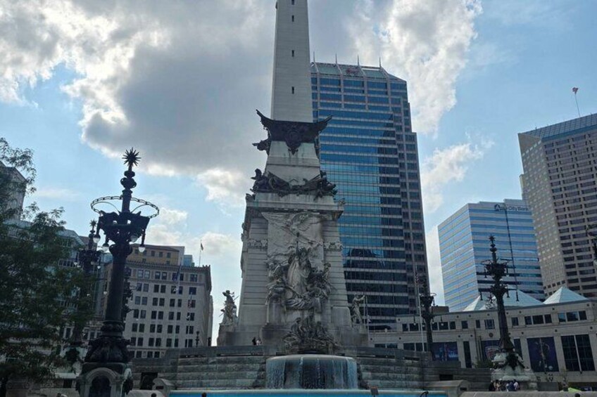 A city square with a central monument, a fountain, and surrounding modern buildings. 2