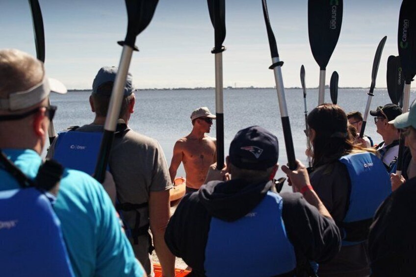 Un grupo de personas en un bote, algunas con chalecos salvavidas, sosteniendo remos y mirando al agua. 4