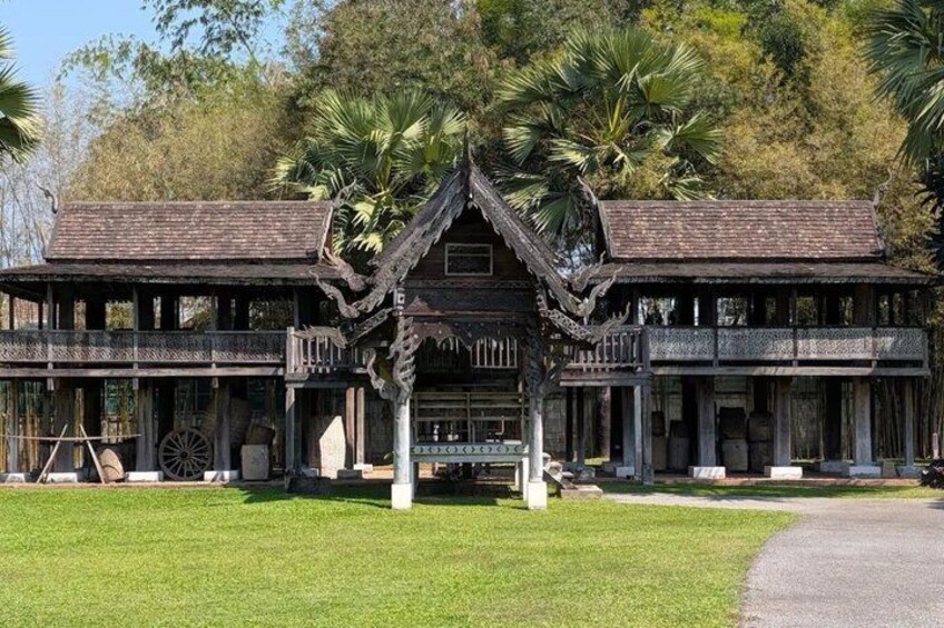 A traditional wooden building with a gabled roof and decorative elements, surrounded by a well-maintained lawn and palm trees. 4