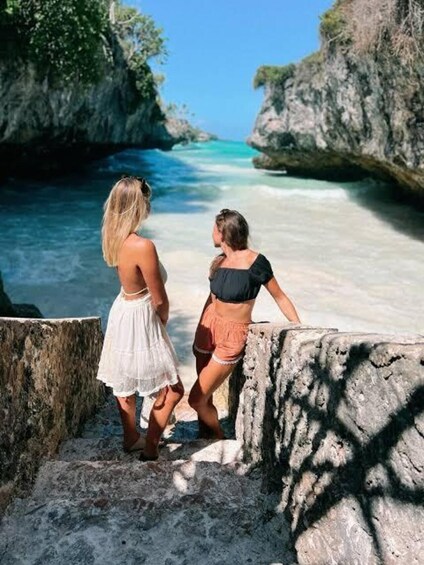 Two people standing on a rocky ledge overlooking a clear blue sea. 3