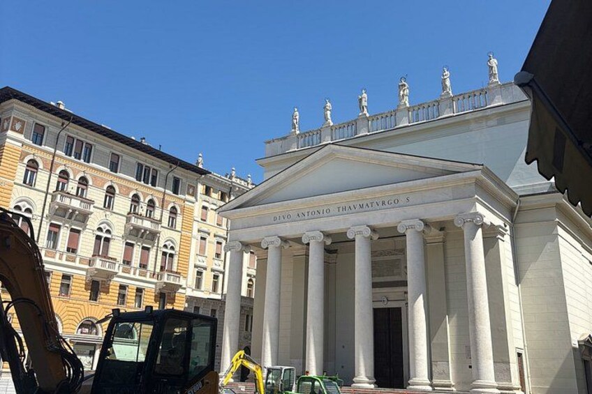 A classical building with columns and statues, construction equipment nearby, and another building in the background. 3