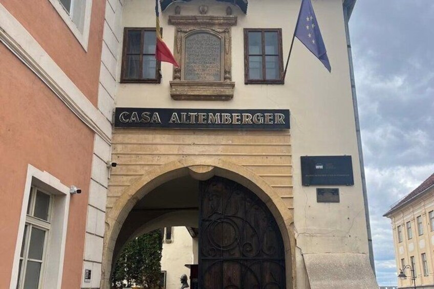 The entrance to Casa Altemberger with a large arched doorway, a plaque, and flags. 2
