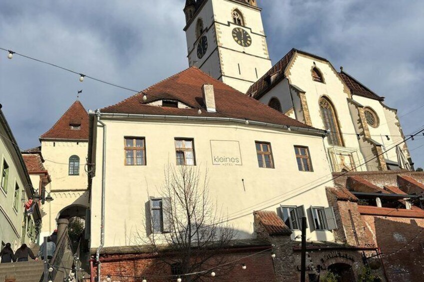 A historic building with a clock tower, a sign reading 'klopos,' and a red-tiled roof. 3