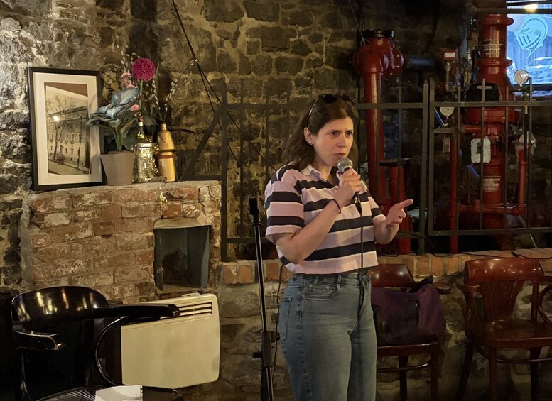 A person speaking into a microphone in a rustic room with stone walls, a fireplace, and vintage furniture. 3