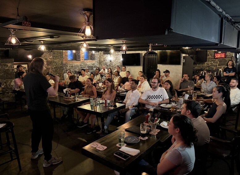 A group of people seated at tables in a dimly lit room with hanging light fixtures. 1
