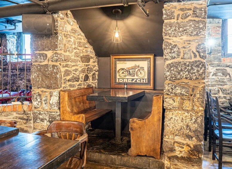 A rustic interior with stone walls, wooden benches, and a framed motorcycle poster. 2