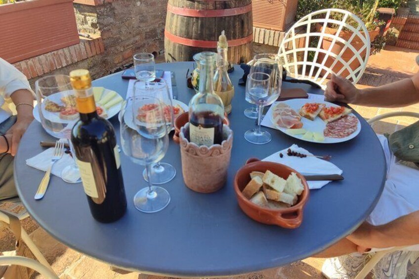 A round table with plates of food, wine glasses, a bottle of wine, and a basket of bread. 3