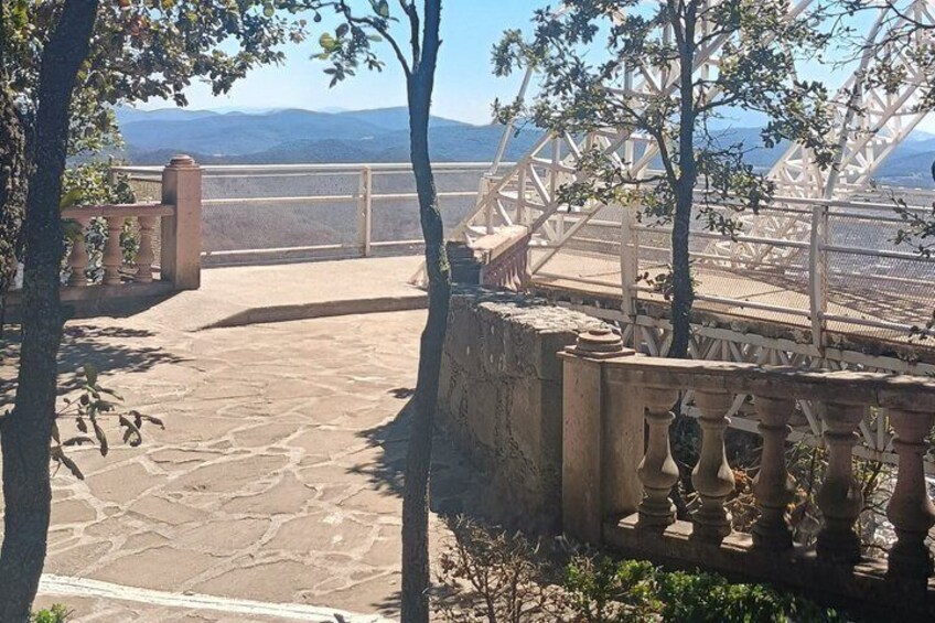 A stone-paved terrace with a railing, trees, and a distant mountain range. 5