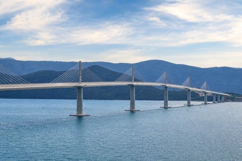 A suspension bridge over a body of water with mountains in the background. 2