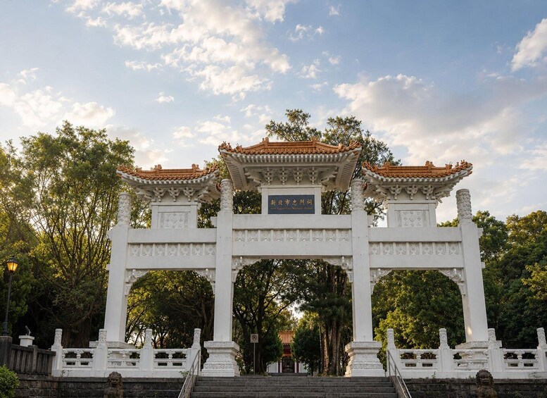 A traditional Chinese gate with ornate roof and columns, surrounded by trees and a clear sky. 4