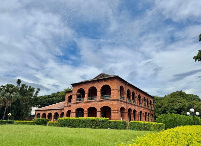 A large brick building with multiple arches and a green roof, surrounded by well-maintained hedges and trees. 3