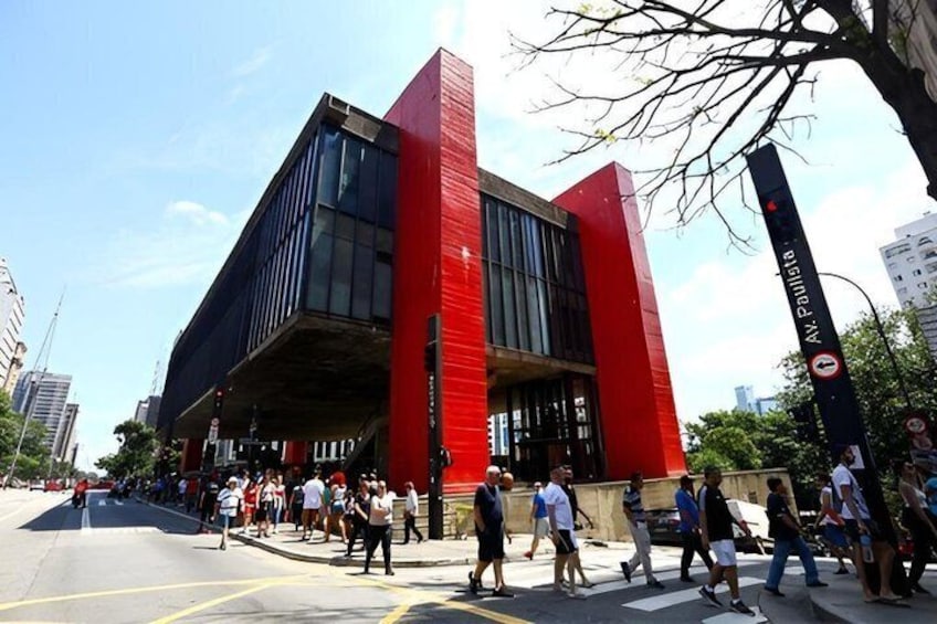 A modern building with a red and black facade, a pedestrian crossing, and a clear blue sky. 1