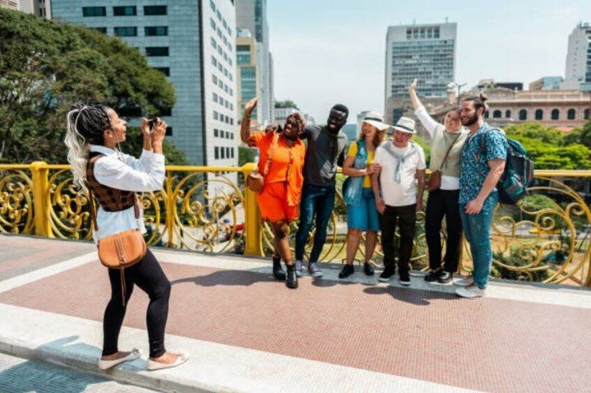 A group of people taking a photo on a bridge with a cityscape in the background. 2