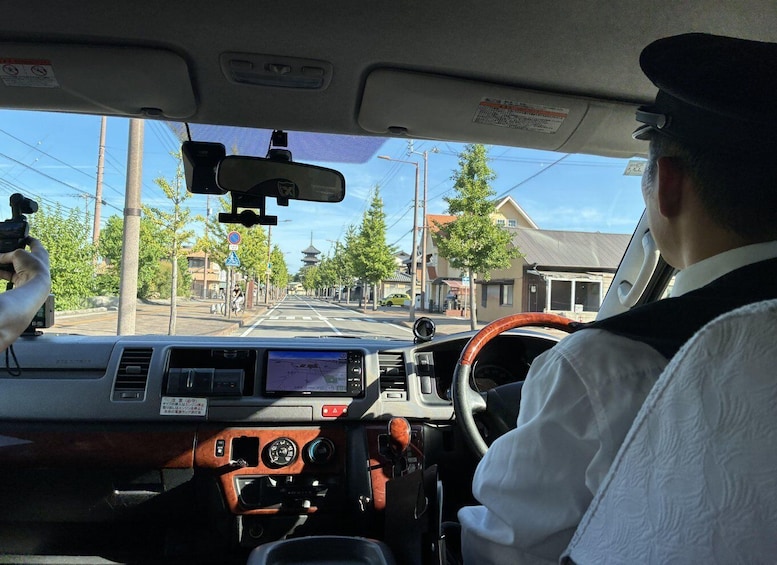 A driver in a vehicle with a dashboard, steering wheel, and rearview mirror. 2
