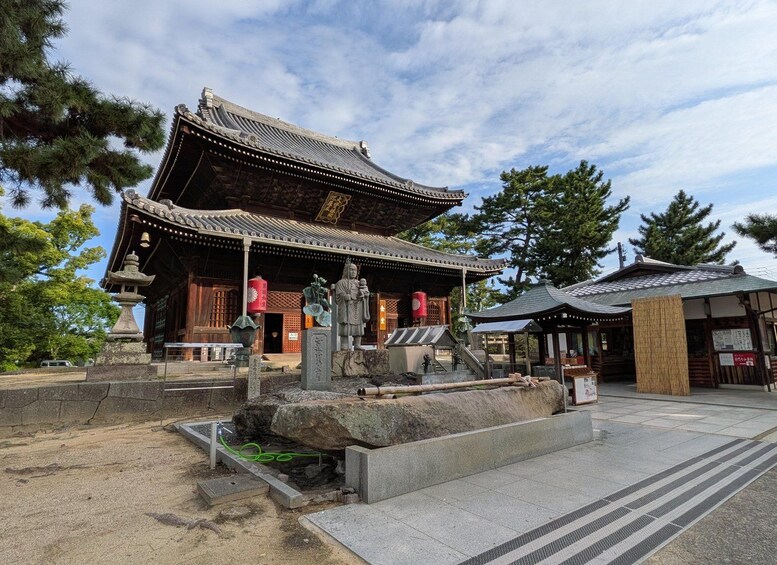 A traditional Japanese temple with a large bell, a statue, and a stone lantern. 5