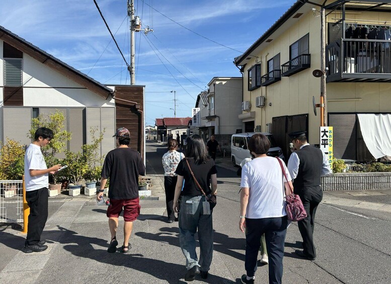 A group of people walking down a street lined with buildings, some with balconies and others with awnings. 4