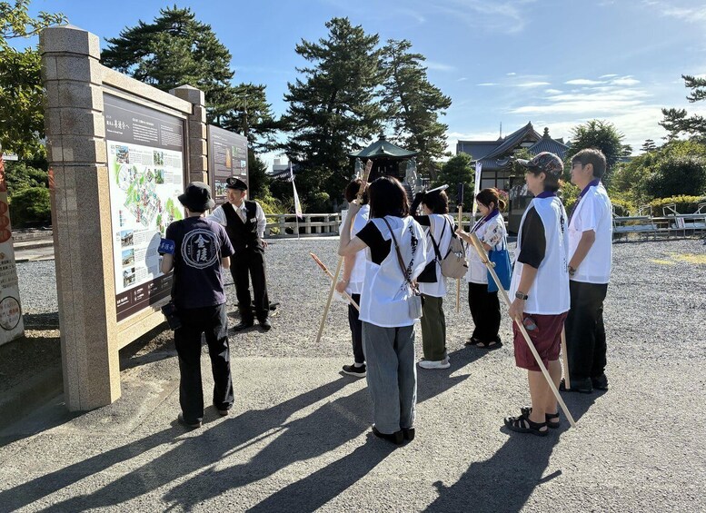 A group of people standing in front of a stone monument with informational plaques, in a park with trees and traditional buildings in the background. 5
