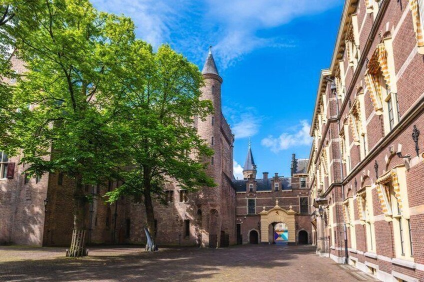 A historic building with a tower, a tree-lined courtyard, and a clear blue sky. 2