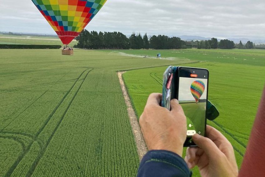 A person taking a photo of a colorful hot air balloon in a green field. 3