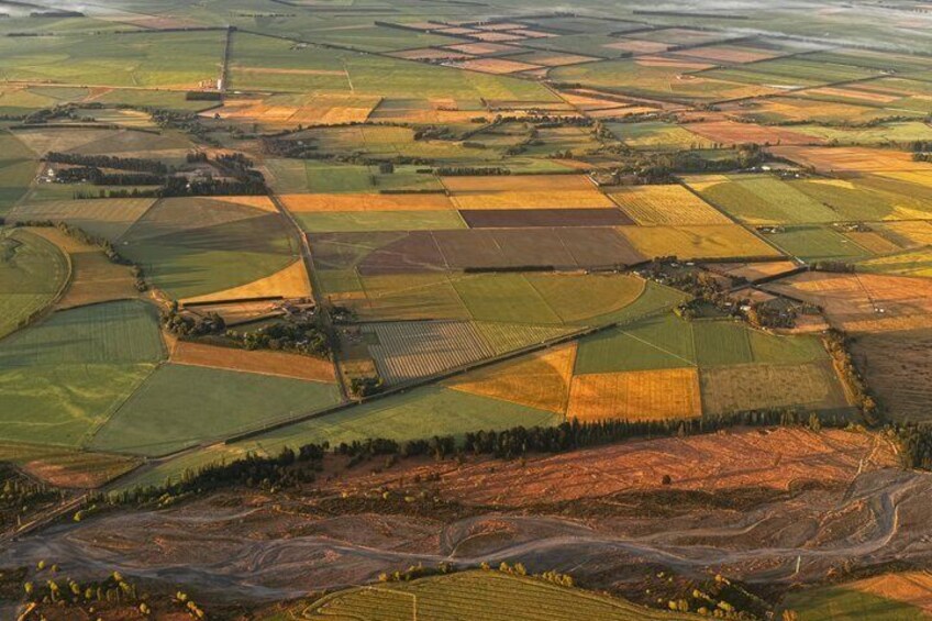 An aerial view of a patchwork of fields with varying colors, indicating different crops or stages of growth, and a small cluster of buildings. 3