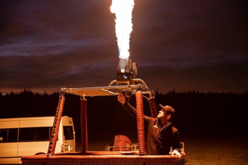 A person operating a large, industrial machine with a visible flame at the top, set against a dark night sky with a forest in the background. 5